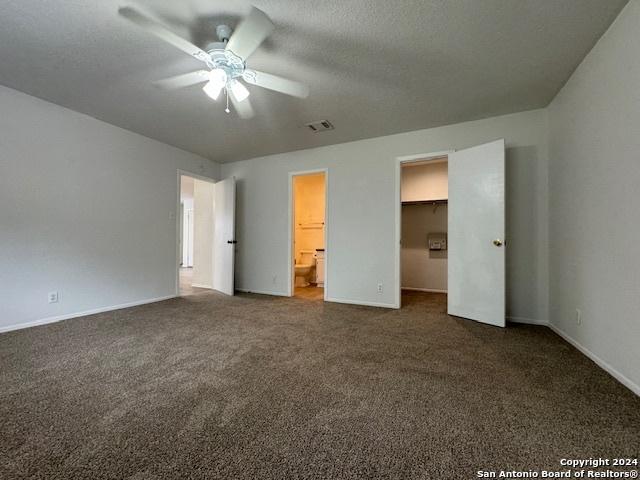 unfurnished bedroom featuring dark carpet, ensuite bathroom, ceiling fan, a spacious closet, and a closet