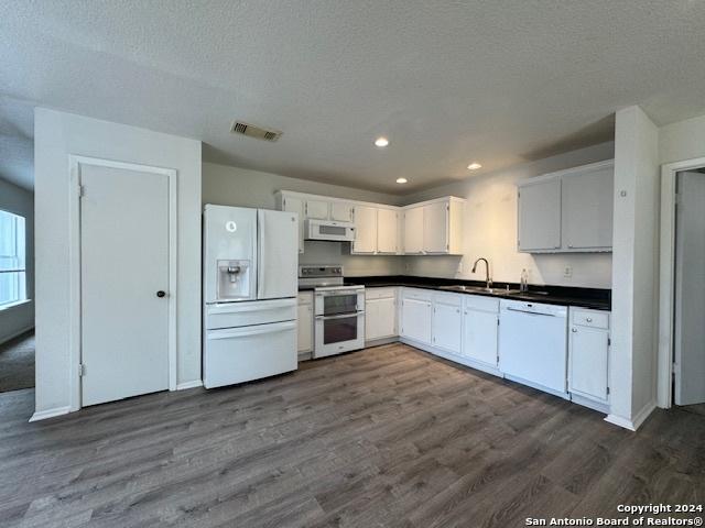 kitchen with a textured ceiling, white appliances, sink, white cabinets, and dark hardwood / wood-style floors