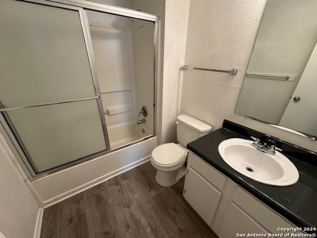 full bathroom with bath / shower combo with glass door, vanity, wood-type flooring, and toilet