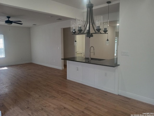 kitchen with sink, dark wood-type flooring, kitchen peninsula, pendant lighting, and ceiling fan with notable chandelier