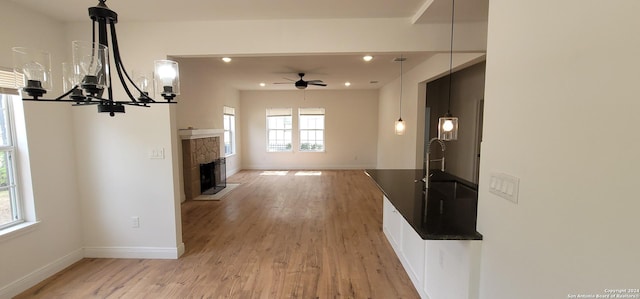 unfurnished living room featuring ceiling fan with notable chandelier, light hardwood / wood-style floors, a stone fireplace, and sink