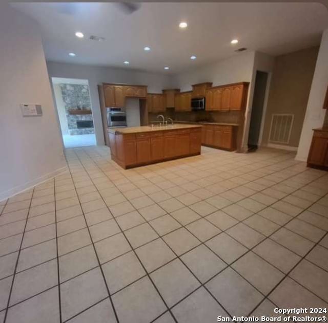 kitchen with appliances with stainless steel finishes, light tile patterned floors, and an island with sink