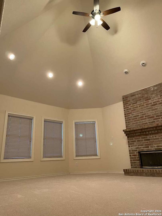 unfurnished living room featuring carpet flooring, lofted ceiling, ceiling fan, a brick fireplace, and brick wall