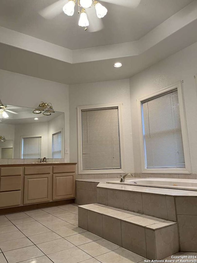 bathroom featuring tiled bath, a raised ceiling, vanity, and ceiling fan