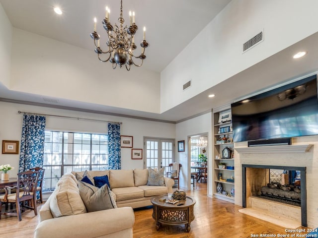 living room featuring a fireplace, a high ceiling, light hardwood / wood-style floors, and an inviting chandelier