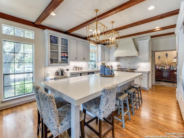 kitchen with a kitchen bar, custom exhaust hood, pendant lighting, white cabinets, and a kitchen island