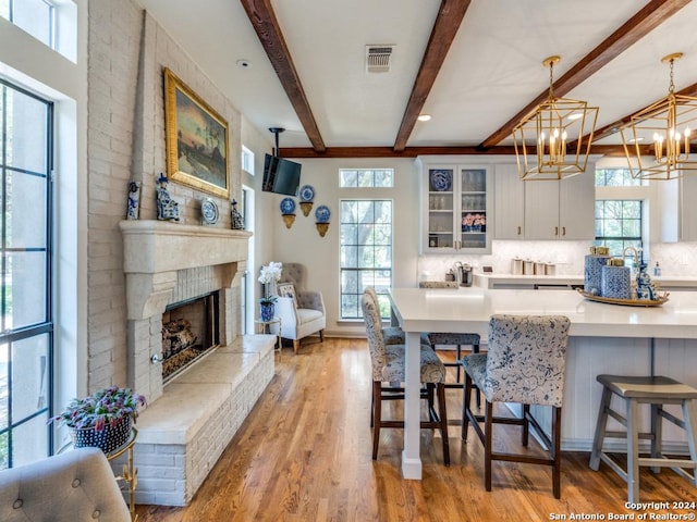 kitchen featuring white cabinetry, a kitchen breakfast bar, pendant lighting, light hardwood / wood-style floors, and a fireplace