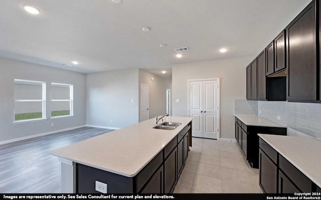 kitchen with sink, tasteful backsplash, a kitchen island with sink, and light tile floors