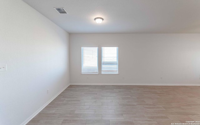 spare room with light wood finished floors, baseboards, and visible vents