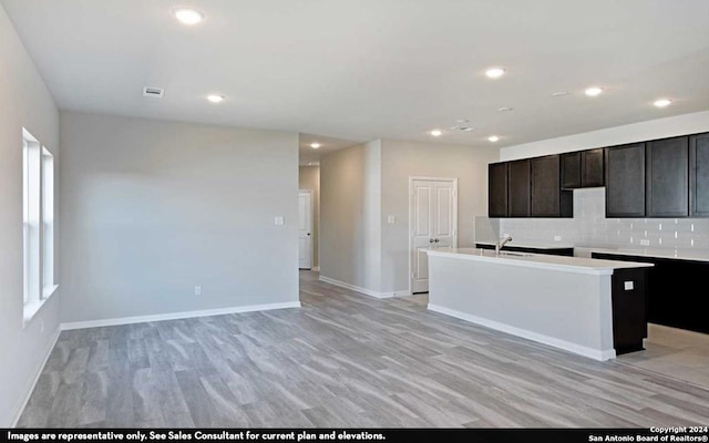 kitchen featuring dark brown cabinetry, light hardwood / wood-style flooring, a center island with sink, tasteful backsplash, and sink