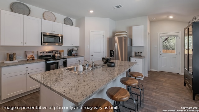 kitchen with light stone countertops, stainless steel appliances, a kitchen island with sink, white cabinetry, and sink