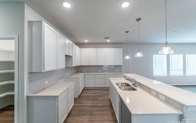 kitchen featuring backsplash, sink, hanging light fixtures, an island with sink, and white cabinets