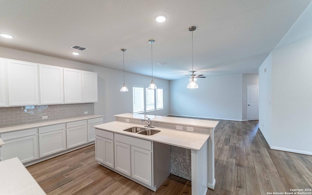 kitchen featuring ceiling fan, backsplash, sink, white cabinetry, and an island with sink