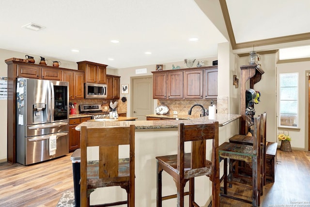 kitchen featuring light hardwood / wood-style flooring, kitchen peninsula, stainless steel appliances, backsplash, and a breakfast bar area