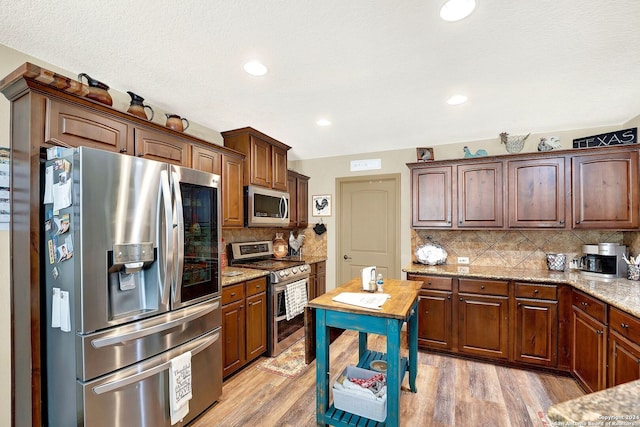 kitchen featuring stainless steel appliances, light hardwood / wood-style flooring, light stone counters, and tasteful backsplash