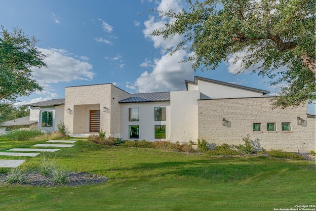 modern home featuring a standing seam roof, metal roof, a front lawn, and stucco siding