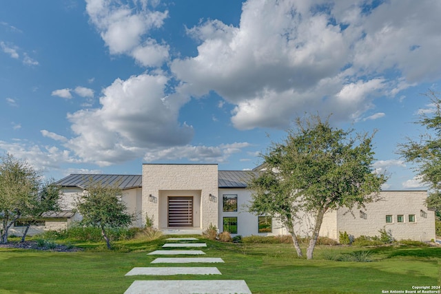 modern home with metal roof, a front lawn, a standing seam roof, and stucco siding