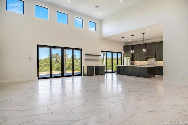 unfurnished living room featuring a towering ceiling, sink, and light tile floors