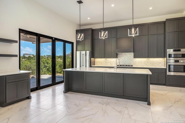 kitchen with appliances with stainless steel finishes, an island with sink, decorative light fixtures, tasteful backsplash, and light tile floors