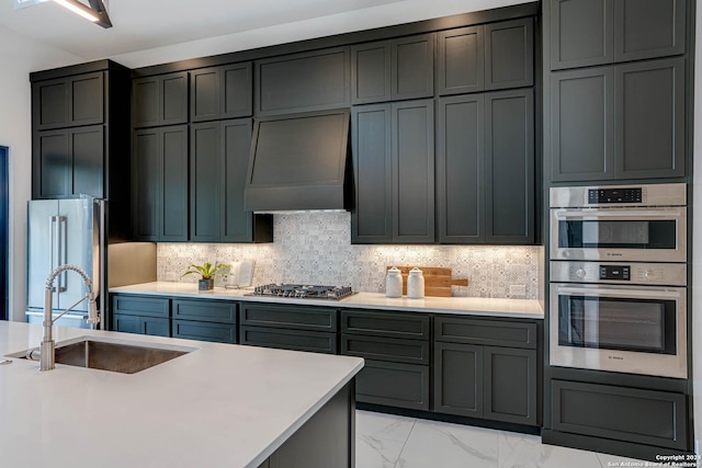 kitchen with a sink, marble finish floor, stainless steel appliances, premium range hood, and backsplash