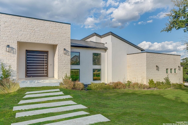 property entrance featuring metal roof, a standing seam roof, a lawn, and stucco siding