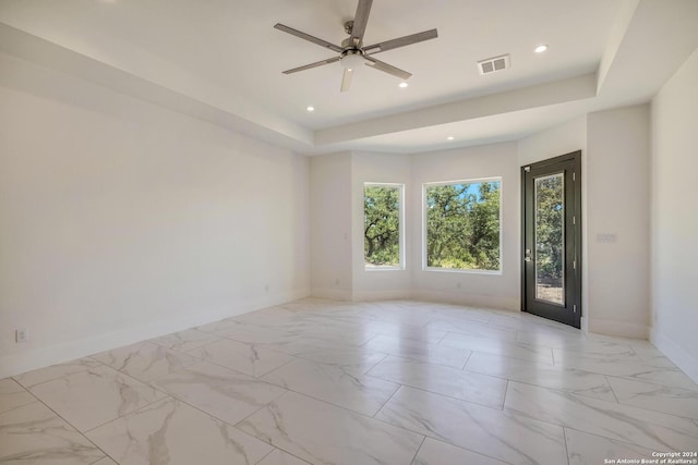 spare room featuring a tray ceiling, ceiling fan, and light tile floors