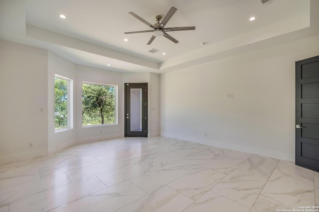 tiled empty room with ceiling fan and a raised ceiling