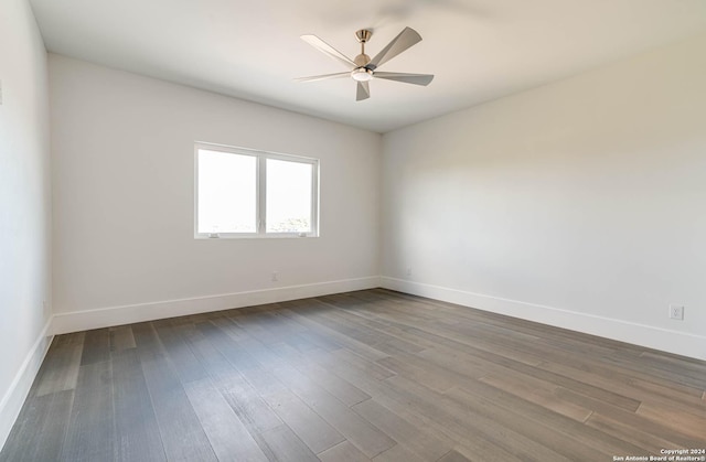 spare room with dark wood-type flooring, a ceiling fan, and baseboards