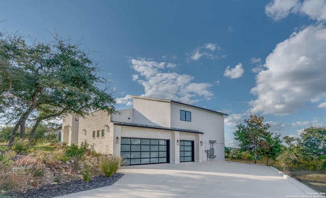 view of side of property featuring concrete driveway, brick siding, an attached garage, and stucco siding