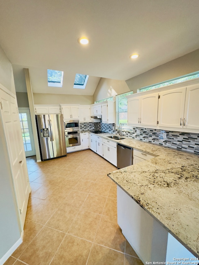 kitchen with tasteful backsplash, stainless steel appliances, lofted ceiling with skylight, light tile floors, and sink