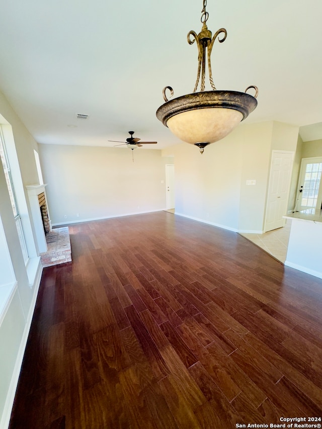 unfurnished living room with wood-type flooring, ceiling fan, and a brick fireplace