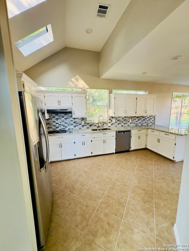 kitchen featuring stainless steel appliances, backsplash, vaulted ceiling with skylight, sink, and light tile flooring