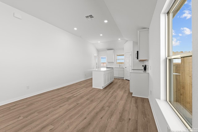 interior space featuring white cabinets, a kitchen island, light hardwood / wood-style floors, and lofted ceiling