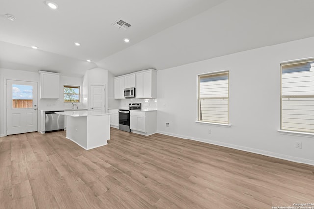 kitchen with backsplash, white cabinets, vaulted ceiling, a kitchen island, and stainless steel appliances