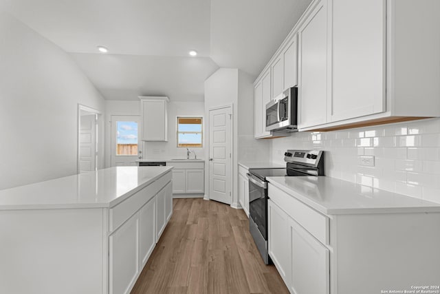 kitchen with white cabinetry, stainless steel appliances, tasteful backsplash, light hardwood / wood-style floors, and vaulted ceiling