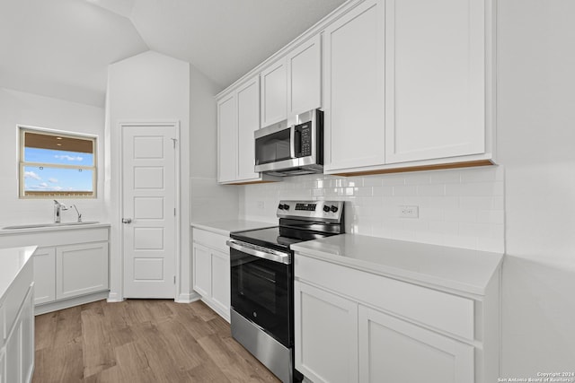 kitchen with white cabinetry, sink, light hardwood / wood-style flooring, lofted ceiling, and appliances with stainless steel finishes