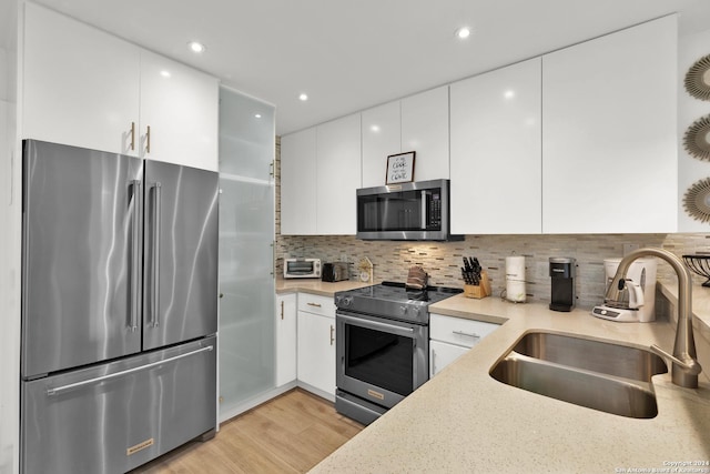 kitchen with white cabinets, sink, decorative backsplash, light wood-type flooring, and stainless steel appliances