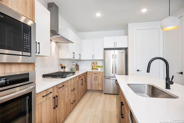 kitchen featuring tasteful backsplash, wall chimney exhaust hood, light hardwood / wood-style flooring, and stainless steel appliances