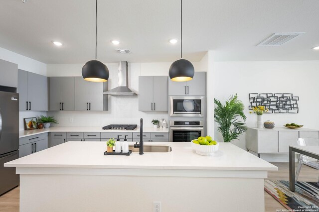 kitchen with gray cabinetry, wall chimney exhaust hood, hanging light fixtures, and appliances with stainless steel finishes