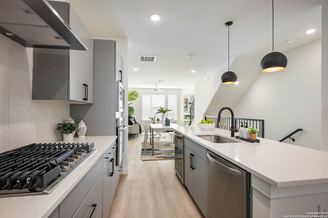 kitchen with sink, hanging light fixtures, light hardwood / wood-style flooring, wall chimney exhaust hood, and appliances with stainless steel finishes