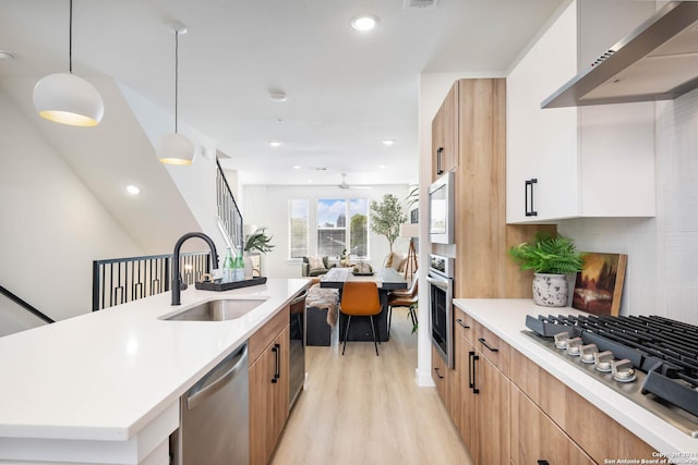 kitchen featuring sink, stainless steel appliances, wall chimney range hood, light hardwood / wood-style flooring, and decorative light fixtures