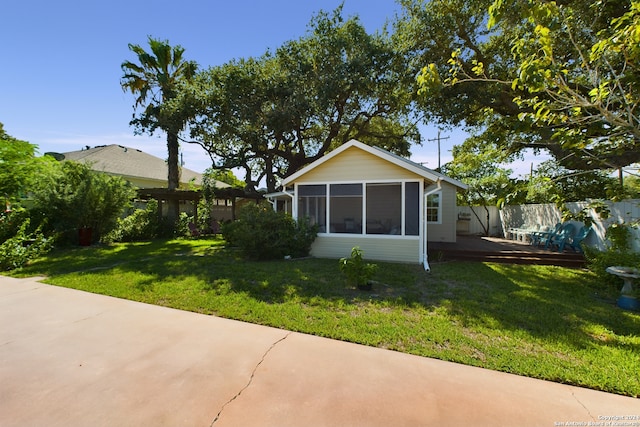 rear view of house with a lawn, a wooden deck, a sunroom, and fence