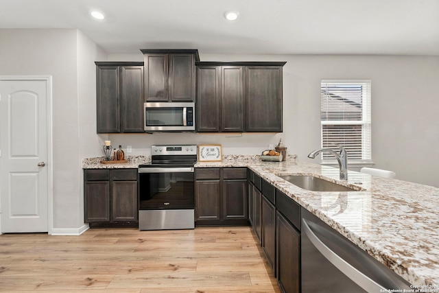 kitchen featuring sink, stainless steel appliances, light stone counters, dark brown cabinets, and light wood-type flooring