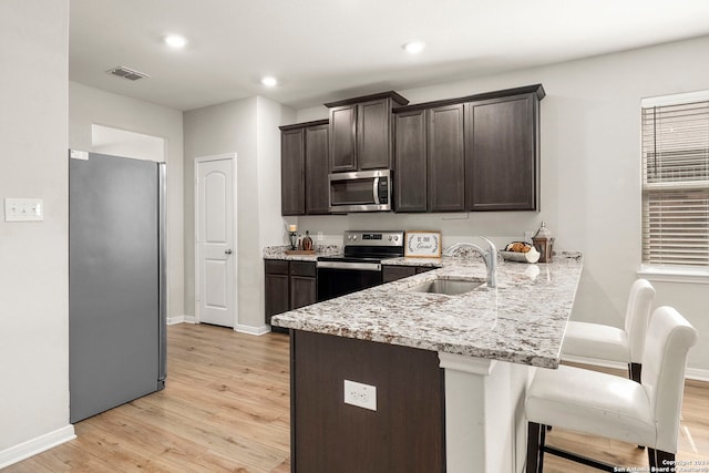 kitchen featuring sink, light stone counters, light hardwood / wood-style flooring, a breakfast bar area, and appliances with stainless steel finishes