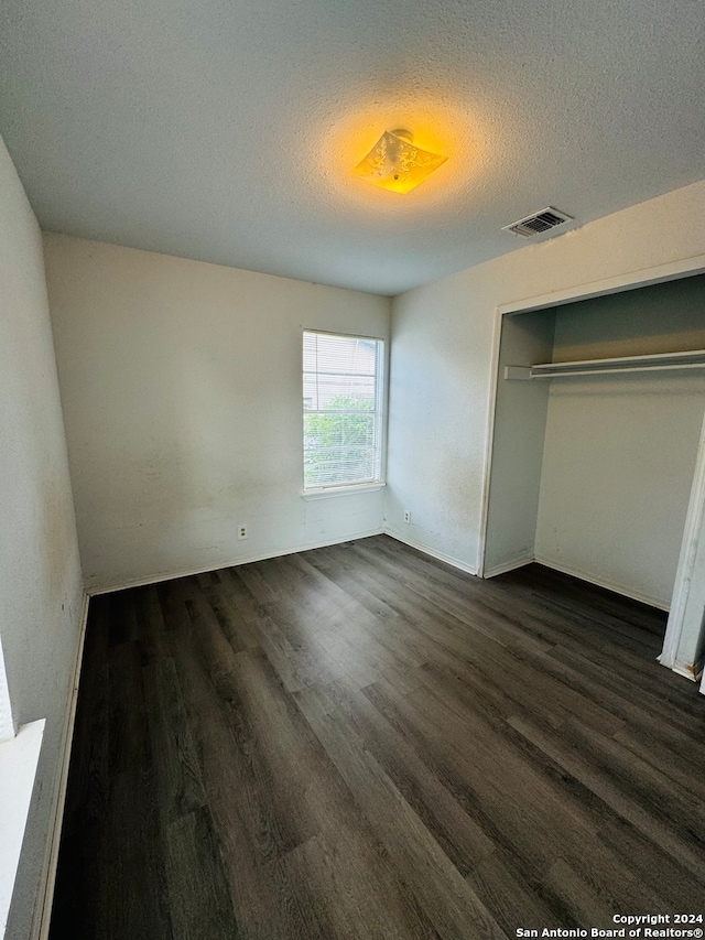 unfurnished bedroom featuring dark wood-type flooring, a closet, and a textured ceiling