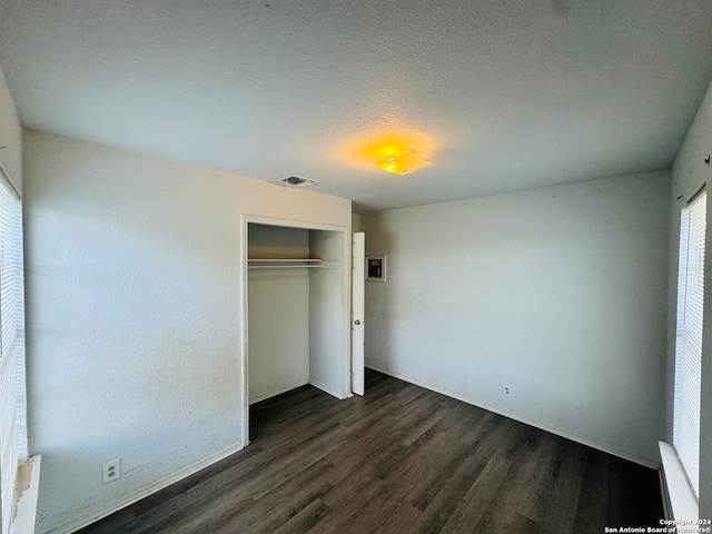 unfurnished bedroom with a textured ceiling, dark wood-type flooring, and a closet