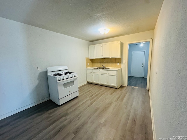 kitchen with gas range gas stove, white cabinets, backsplash, hardwood / wood-style floors, and sink