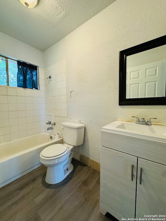 full bathroom featuring a textured ceiling, hardwood / wood-style floors, tiled shower / bath combo, vanity, and toilet