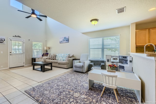 living room with ceiling fan, sink, a high ceiling, a textured ceiling, and light tile patterned floors