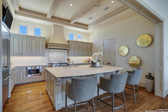 kitchen with appliances with stainless steel finishes, custom range hood, a kitchen island with sink, and a kitchen breakfast bar